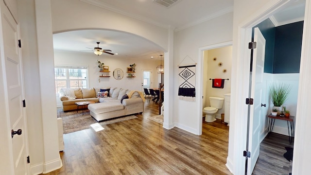 living area featuring crown molding, visible vents, arched walkways, and wood finished floors