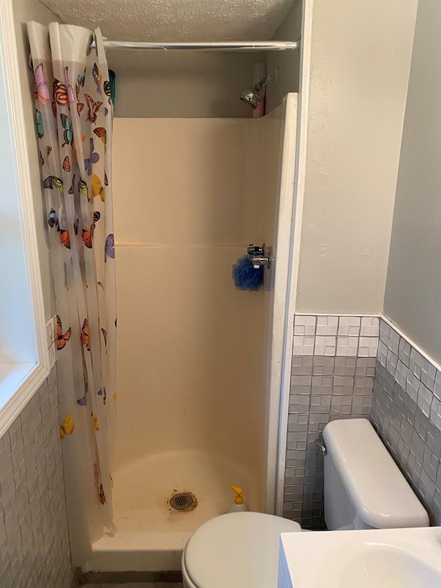 bathroom with a textured ceiling, toilet, tile walls, and walk in shower