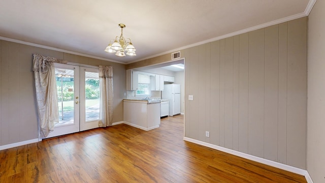 unfurnished dining area with french doors, wood finished floors, a chandelier, baseboards, and ornamental molding