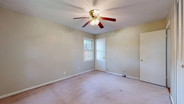empty room featuring light colored carpet, a ceiling fan, and baseboards