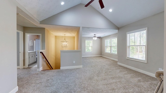 unfurnished living room featuring baseboards, vaulted ceiling, light colored carpet, and ceiling fan with notable chandelier