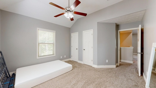 carpeted bedroom featuring two closets, baseboards, lofted ceiling, and ceiling fan