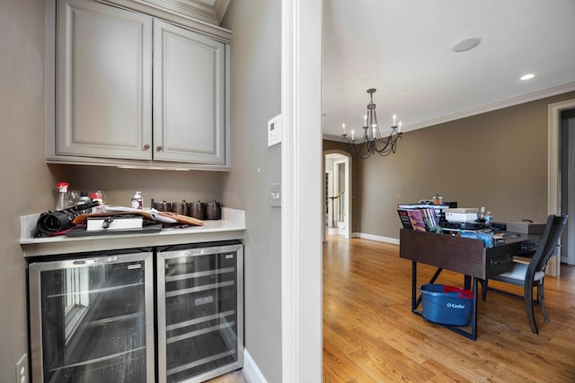 bar with hanging light fixtures, crown molding, light hardwood / wood-style floors, and beverage cooler