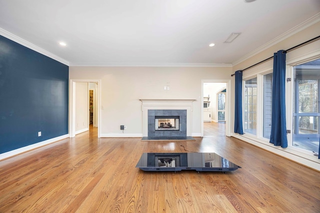 unfurnished living room with a tiled fireplace, crown molding, and light hardwood / wood-style floors