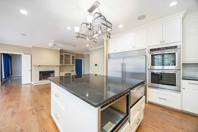 kitchen with appliances with stainless steel finishes, white cabinetry, hanging light fixtures, light hardwood / wood-style floors, and crown molding