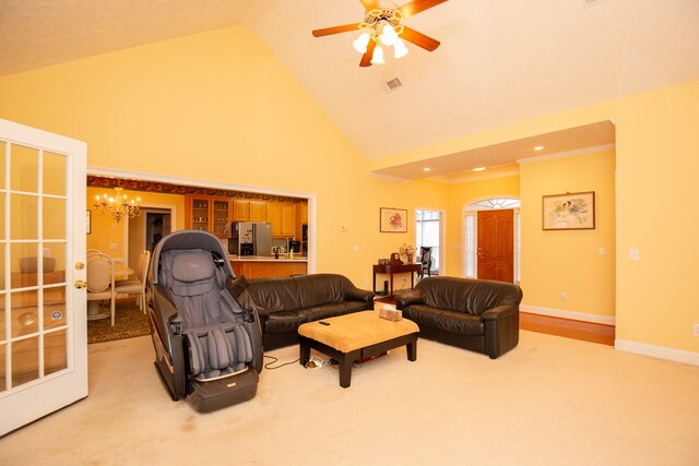 carpeted living room featuring ceiling fan with notable chandelier and high vaulted ceiling