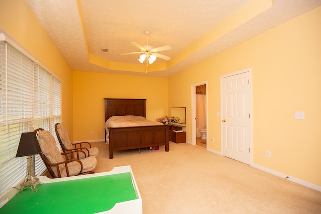 bedroom featuring carpet flooring, ensuite bath, a textured ceiling, a raised ceiling, and ceiling fan