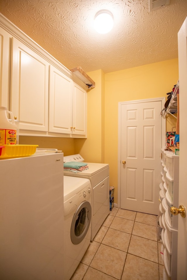 laundry room featuring washer and clothes dryer, light tile patterned flooring, cabinets, and a textured ceiling