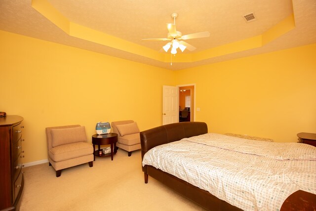 carpeted bedroom with ceiling fan, a textured ceiling, and a tray ceiling