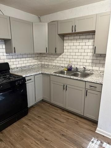 kitchen featuring dark hardwood / wood-style flooring, backsplash, gray cabinetry, sink, and black gas stove