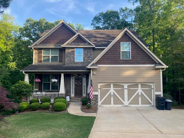 craftsman inspired home with covered porch, driveway, a garage, a front lawn, and stone siding