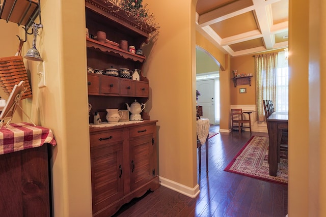 hallway featuring dark wood-style flooring, arched walkways, baseboards, beamed ceiling, and coffered ceiling