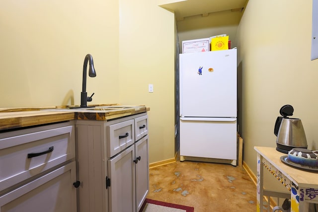 kitchen with baseboards, freestanding refrigerator, a sink, and concrete flooring
