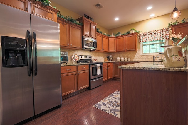 kitchen with dark wood-type flooring, brown cabinetry, appliances with stainless steel finishes, and light stone countertops