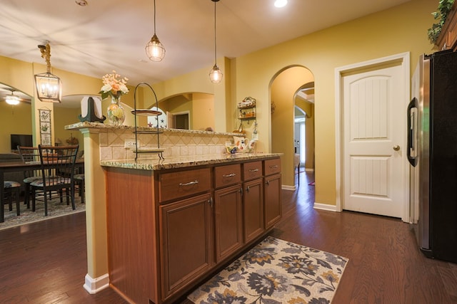 kitchen with backsplash, dark wood-style flooring, pendant lighting, light stone counters, and freestanding refrigerator