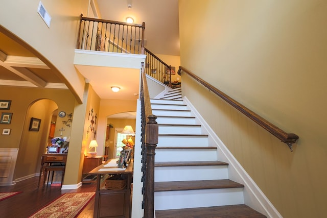 stairway with arched walkways, a high ceiling, visible vents, and wood finished floors