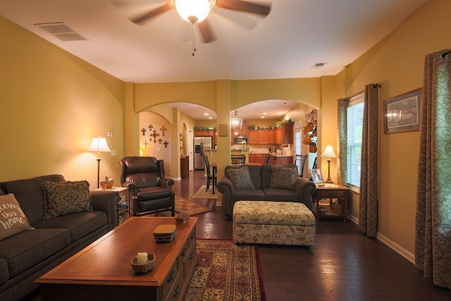 living area featuring arched walkways, ceiling fan, dark wood-style flooring, and visible vents