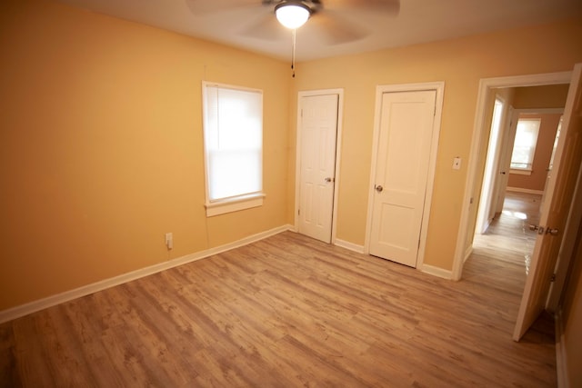 unfurnished bedroom featuring ceiling fan, multiple closets, and light wood-type flooring