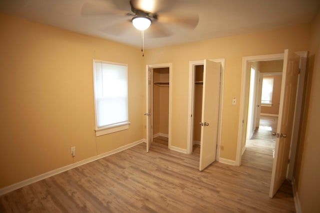 unfurnished bedroom featuring ceiling fan, light hardwood / wood-style flooring, and two closets