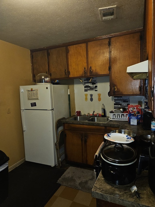 kitchen featuring a sink, dark countertops, visible vents, freestanding refrigerator, and under cabinet range hood