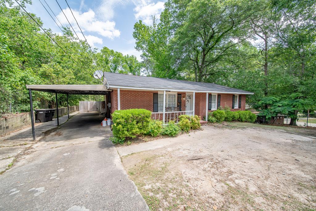 ranch-style house with a porch, brick siding, fence, aphalt driveway, and an attached carport