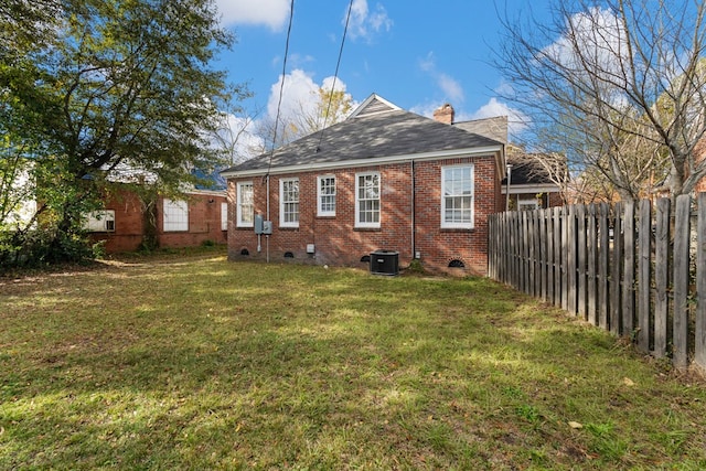 rear view of property with central AC unit and a yard