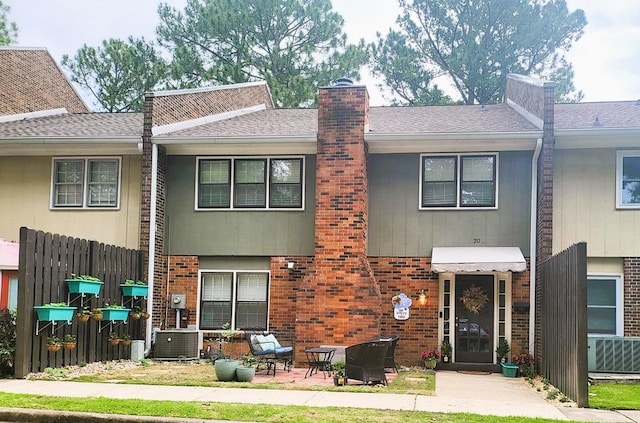 townhome / multi-family property with brick siding, fence, a chimney, and roof with shingles