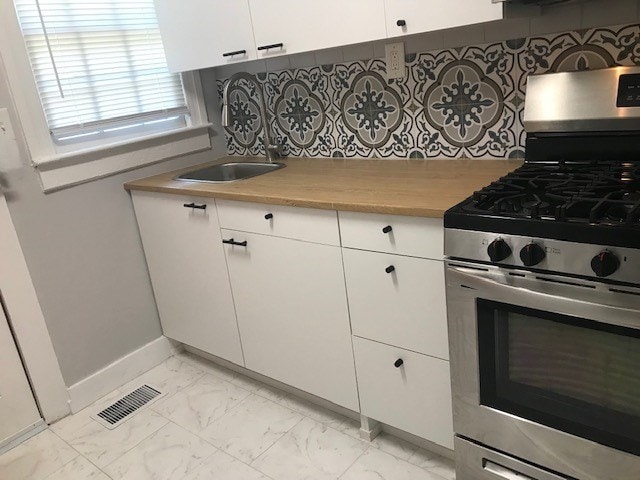 kitchen featuring white cabinets, gas stove, sink, and backsplash