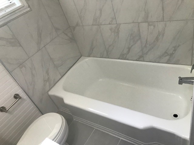 bathroom featuring tile patterned flooring, a tub to relax in, and toilet