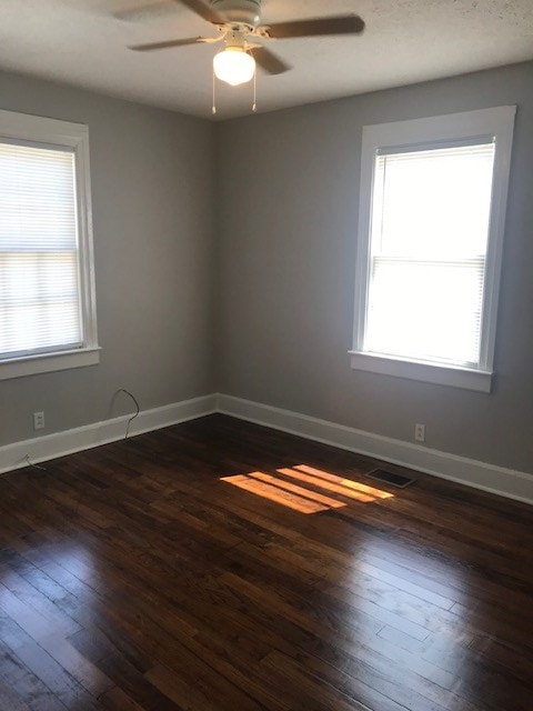 unfurnished room featuring dark wood-type flooring, ceiling fan, and a healthy amount of sunlight