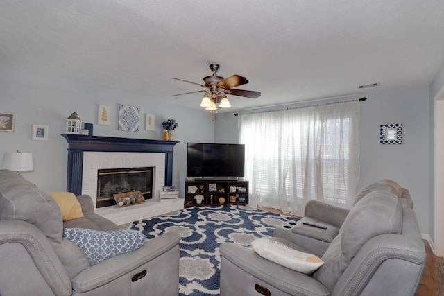 living room with ceiling fan, a brick fireplace, and wood finished floors