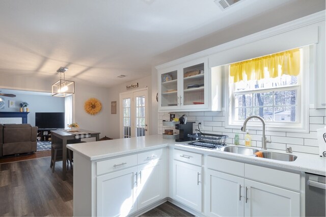 kitchen with a sink, a peninsula, glass insert cabinets, tasteful backsplash, and light countertops