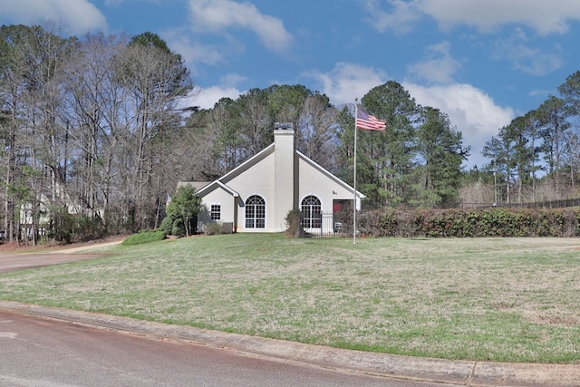 view of side of home with a yard, a chimney, stucco siding, and view of wooded area