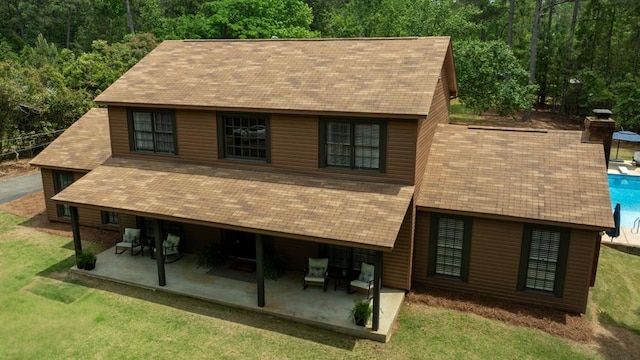 exterior space with a front lawn, a patio area, a shingled roof, and a pool