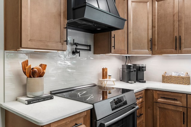 kitchen featuring tasteful backsplash, stainless steel electric stove, brown cabinets, light countertops, and custom range hood