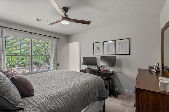 carpeted bedroom featuring a textured ceiling, visible vents, baseboards, and a ceiling fan