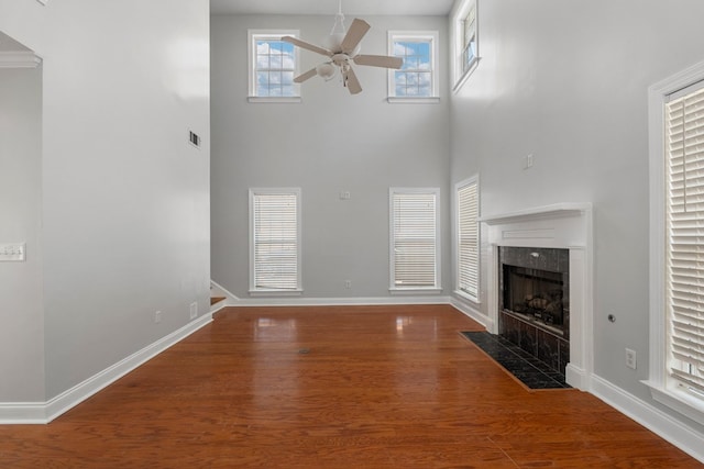 unfurnished living room featuring ceiling fan, a premium fireplace, hardwood / wood-style floors, and a high ceiling