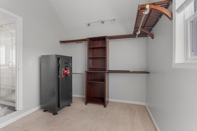 walk in closet with light colored carpet and vaulted ceiling