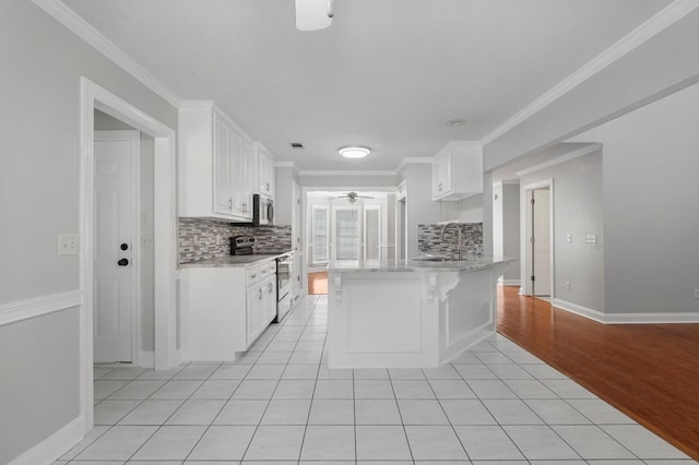 kitchen with stainless steel appliances, light tile patterned floors, tasteful backsplash, white cabinetry, and ornamental molding