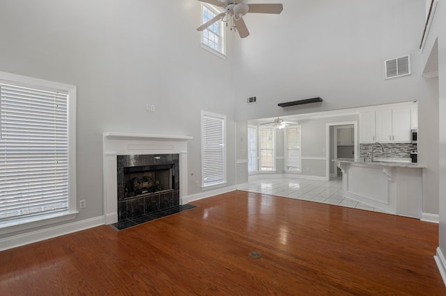 unfurnished living room featuring a towering ceiling, a premium fireplace, sink, and light hardwood / wood-style floors