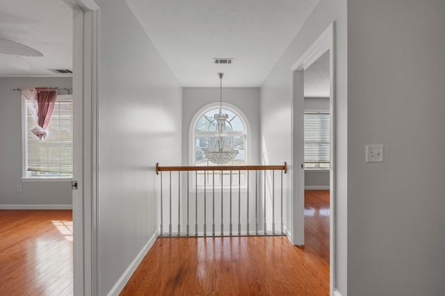 corridor with an inviting chandelier, light hardwood / wood-style floors, and a textured ceiling