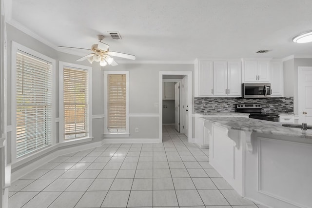 kitchen featuring backsplash, stainless steel appliances, light stone counters, white cabinetry, and light tile patterned flooring