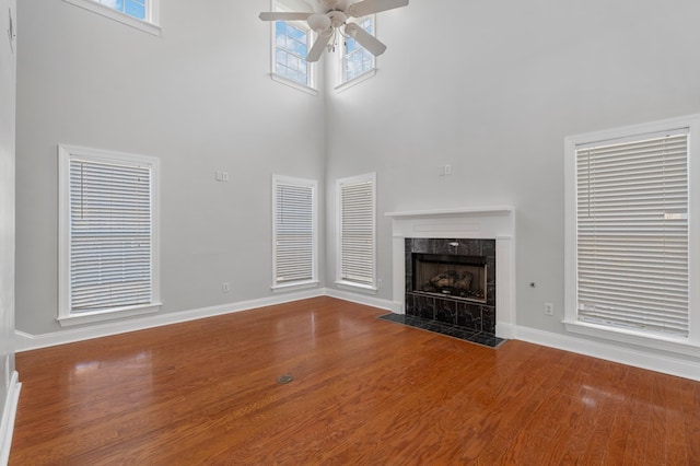 unfurnished living room featuring a fireplace, a towering ceiling, ceiling fan, wood-type flooring, and plenty of natural light