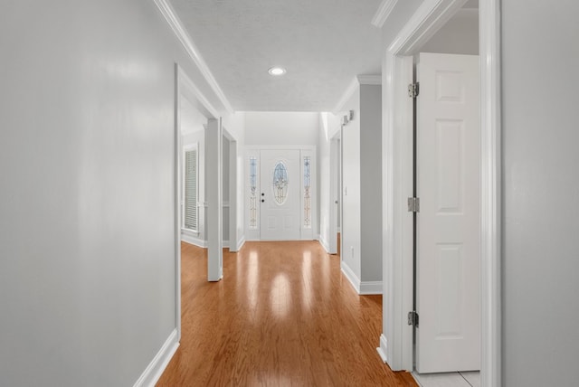 hallway featuring light wood finished floors, crown molding, and baseboards