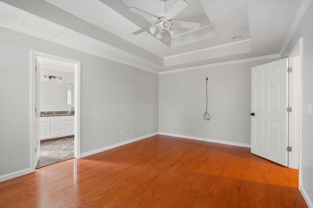 unfurnished bedroom with ensuite bathroom, a raised ceiling, hardwood / wood-style floors, ceiling fan, and crown molding