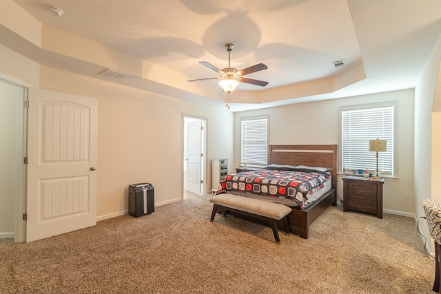 carpeted bedroom with a raised ceiling, a ceiling fan, and baseboards