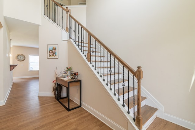 stairway featuring wood finished floors, baseboards, and a towering ceiling