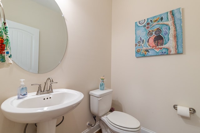 half bathroom with baseboards, toilet, and a sink
