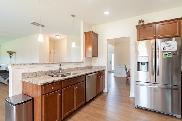kitchen featuring appliances with stainless steel finishes, a sink, light stone countertops, light wood-style floors, and a wainscoted wall
