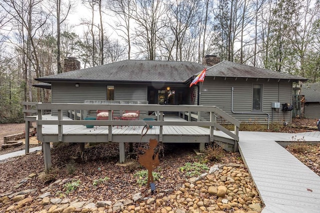 back of house with a wooden deck, a chimney, and a shingled roof